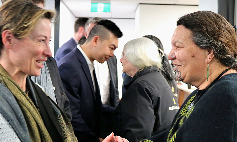 Two women smiling at each other as a man and woman hongi in the background