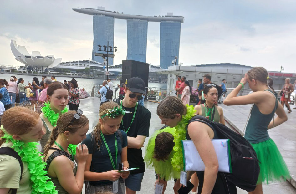 nine of the divers wearing green leis and looking at instructions with the Singapore skyline behind them