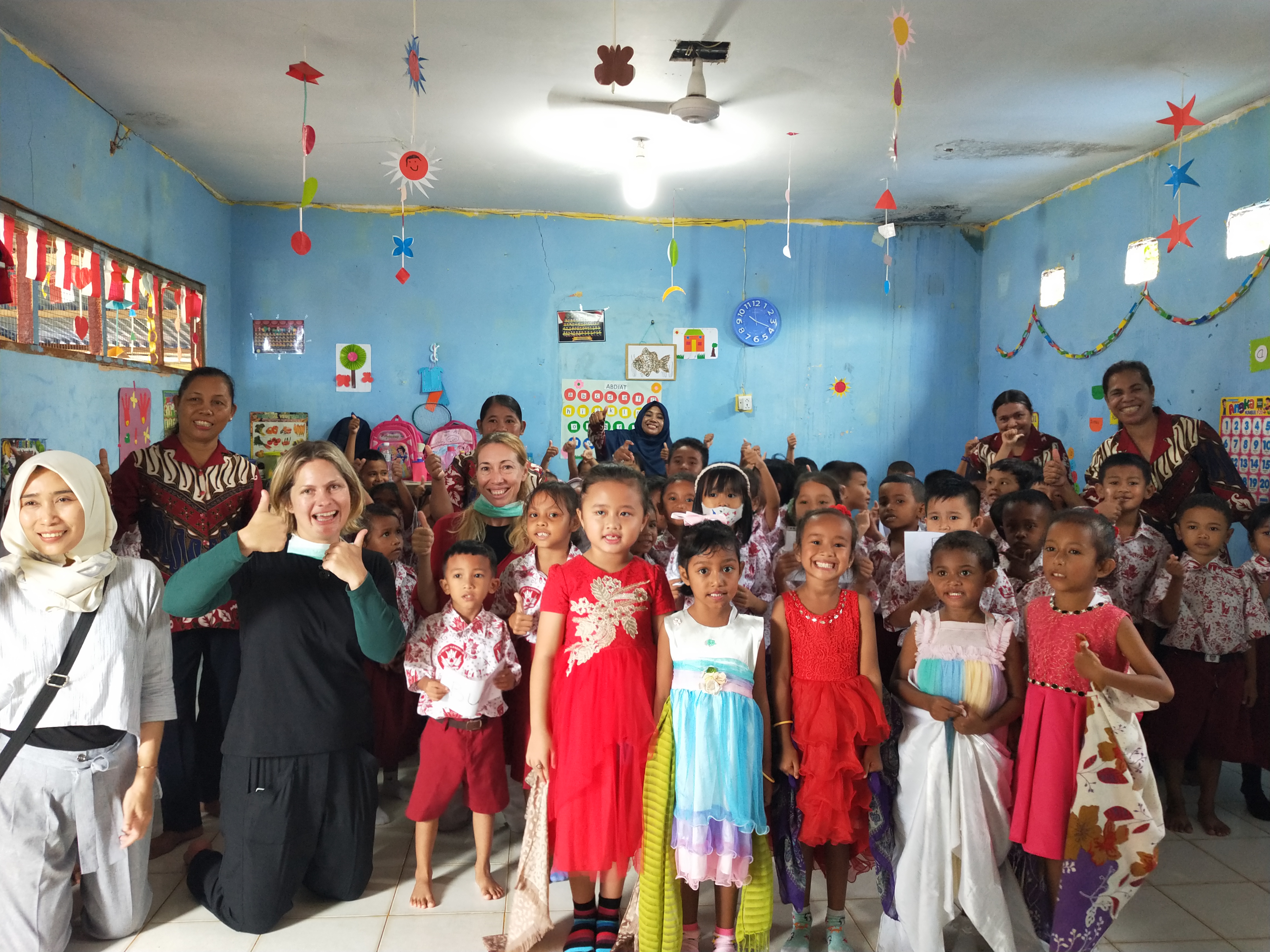 Christey posing in a colourful classroom full of kids, teachers and decorations