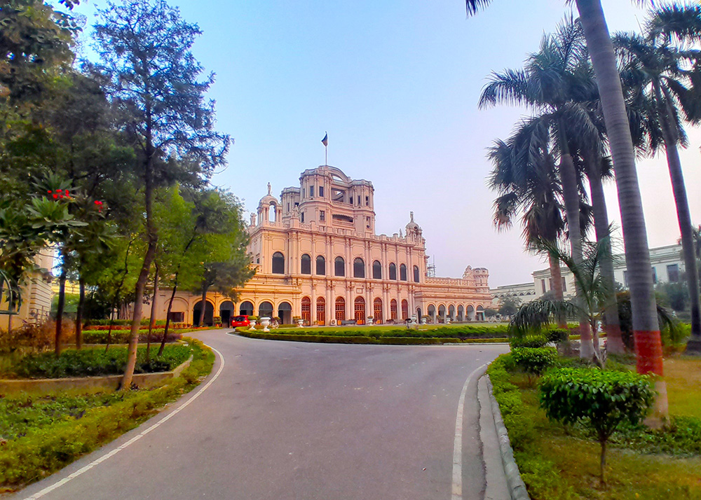 A photo looking down a tree-lined driveway at an ornate apricot coloured building