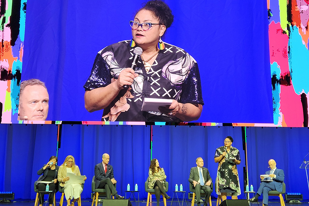 Former Labour Party MP Louisa Wall on stage talking into a microphone with a panel of six fellow panelists