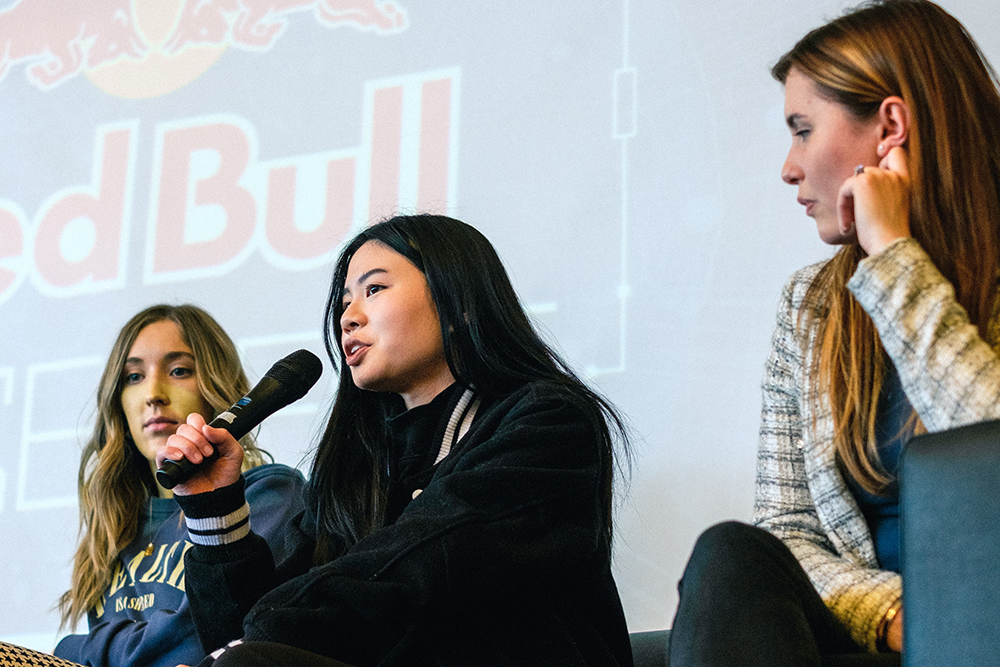 Magdaline speaking into a microphone as part of a panel of speakers