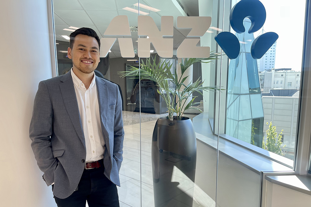Sam Brosnahan standing in front of a glass door with the ANZ logo on it