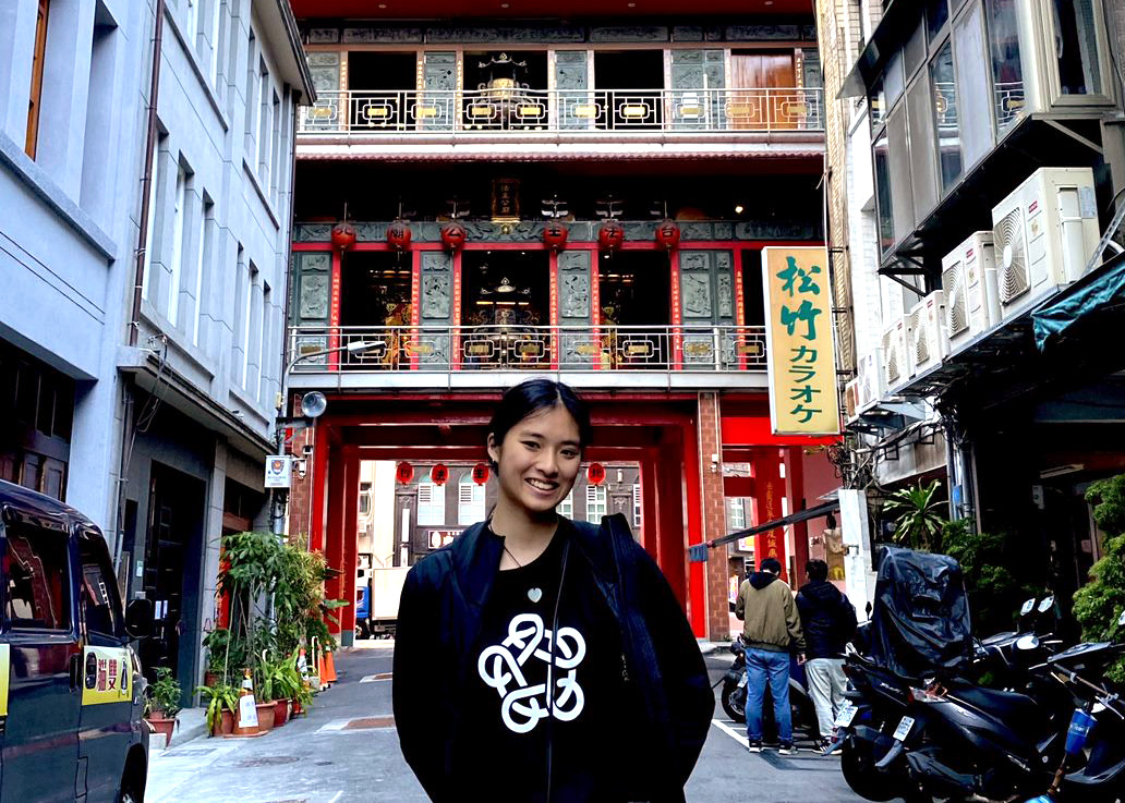 sarah standing in front of a traditional-chinese-looking building wearing an Asia New Zealand Foundation website