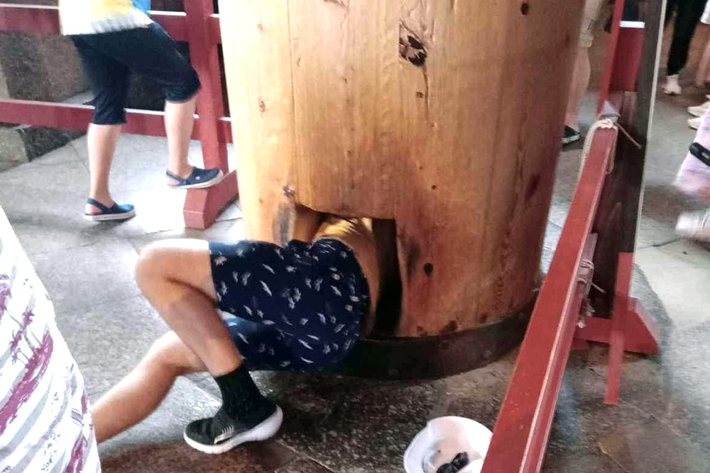 A man (Ned) trying to squeeze through a hole in a pillar and by doing so gain some good luck