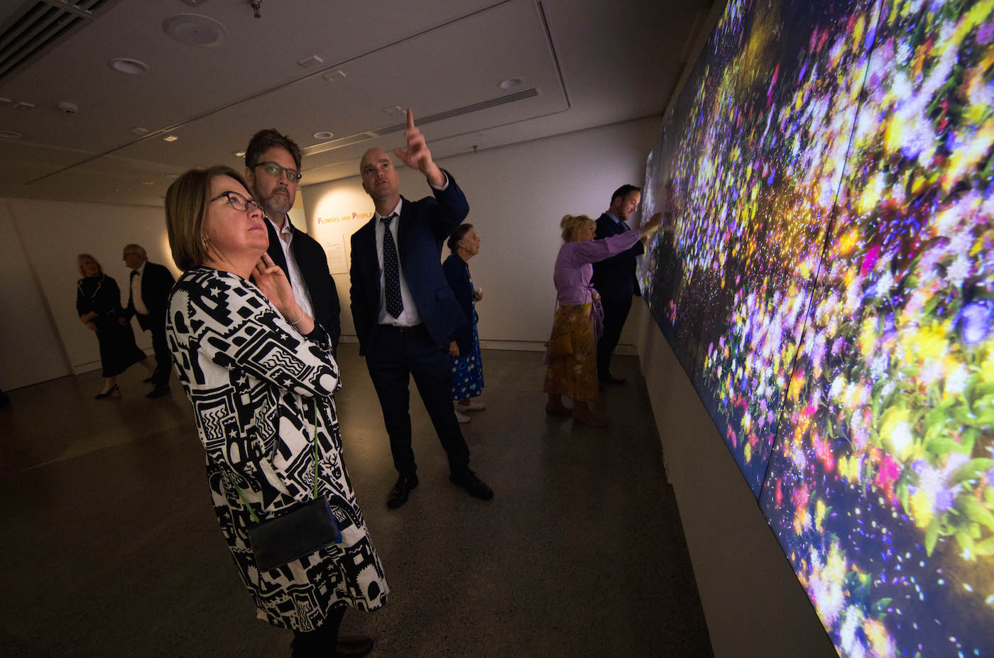Three people looking at the artwork Flowers and people - Gold