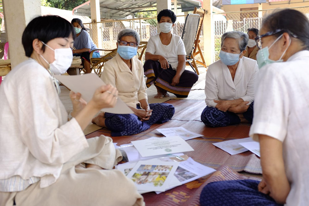 Passawee sitting on a mat with a group of women looking at documents