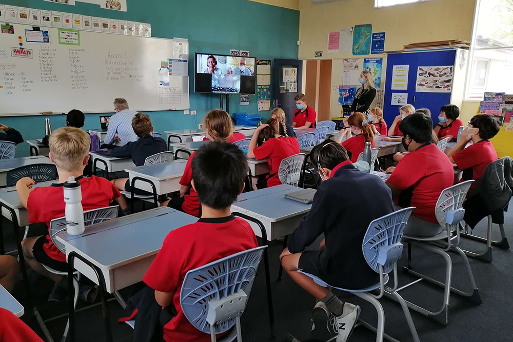 A classroom of students sitting at their desks looking at a screen