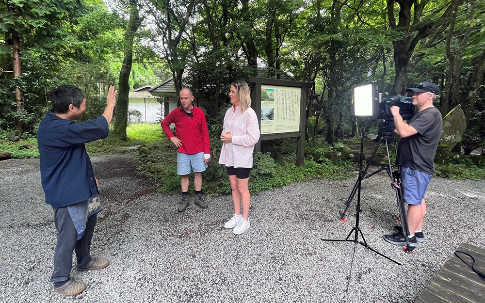 Juliet Speedy standing in a wooded area interviewing a man on camera
