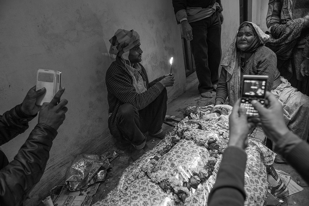 People using their phone cameras to take photos of a woman mourning over the body of a loved one.