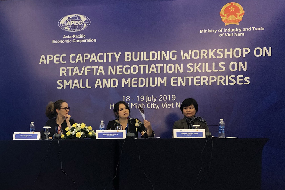 Justine speaking as part of a panel with two others with a sign behind them reading APEC Capability Workshop