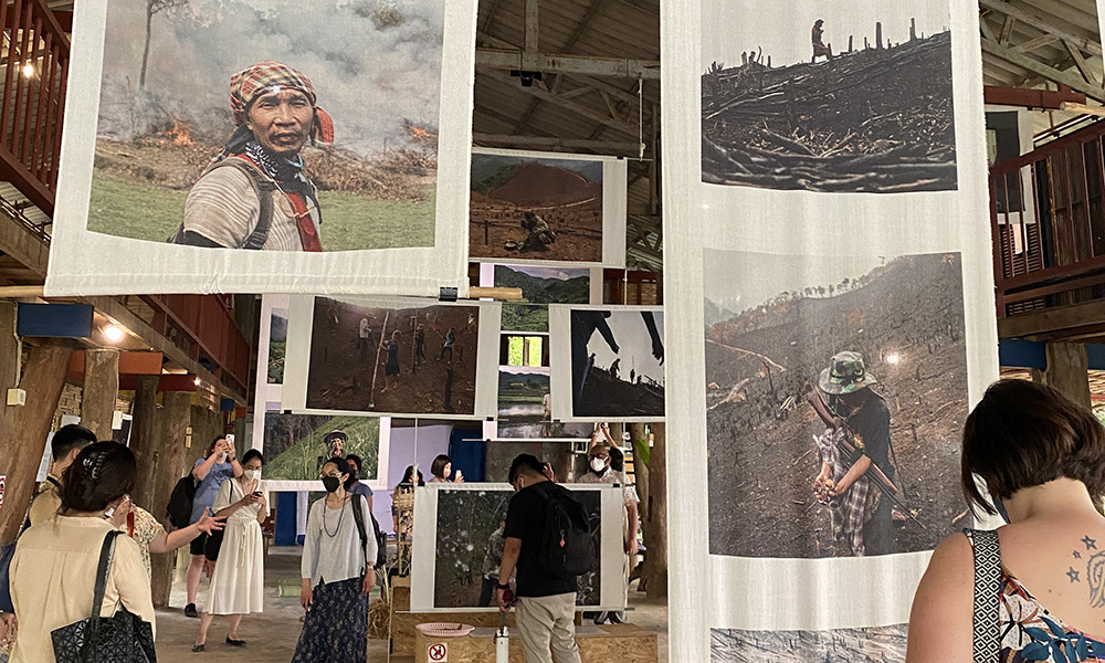 People in a gallery with photos printed on fabric hanging from the ceiling