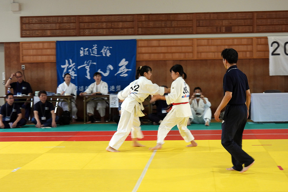 Two women in mid bout, watched on by judges