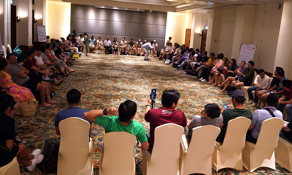A shot taking in an entrire conference room with people sitting in chairs around its edge