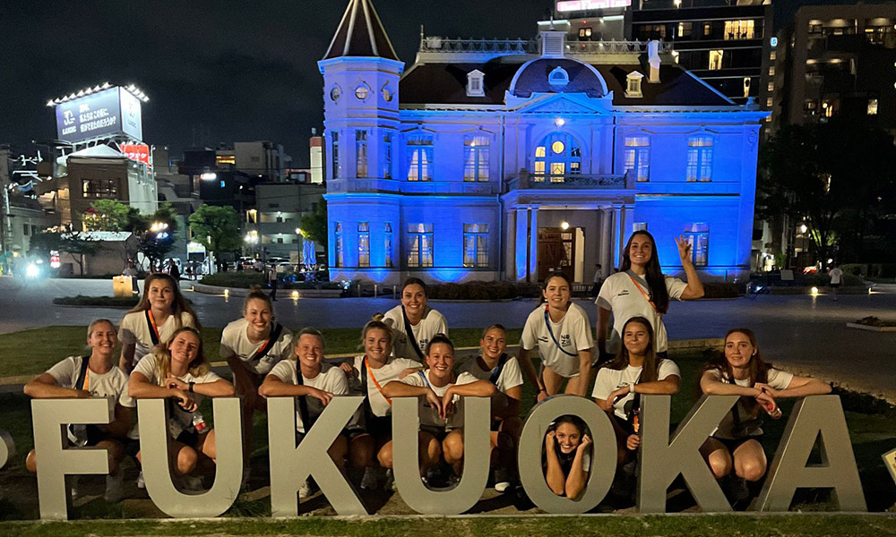 The team posing behind a large Fukuoka sign