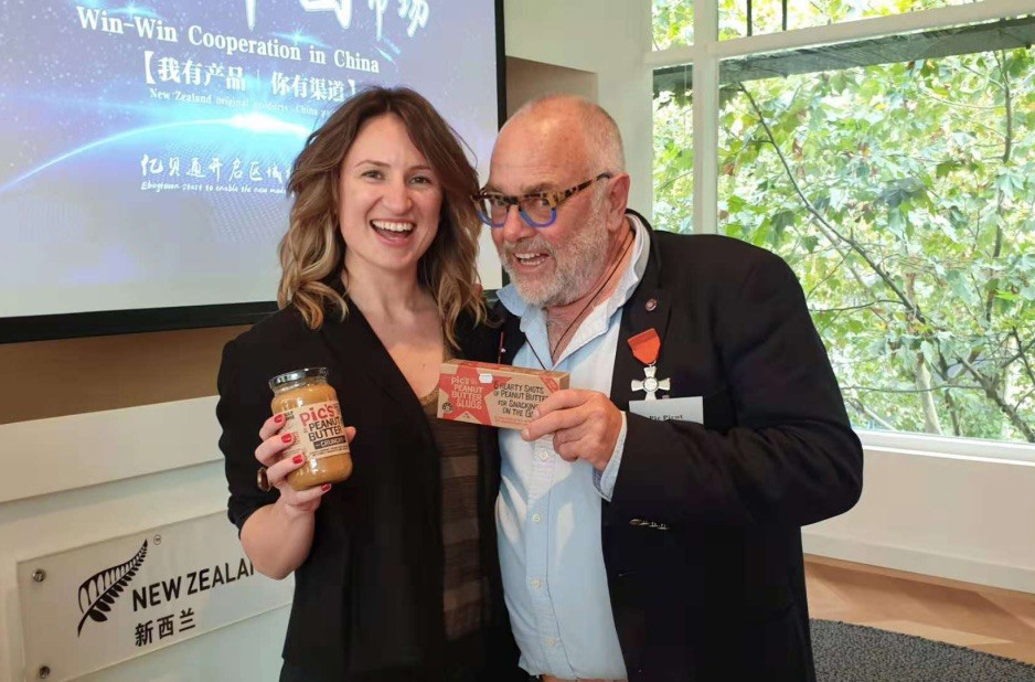 Eleni holding a jar of Pic's peanut butter, standing beside a man holding a box of Pic's Peanut butter fudge