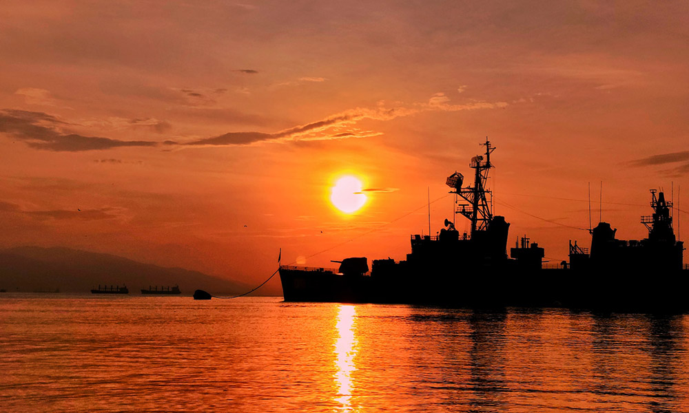A destryoer at anchor with the sun rising in the background