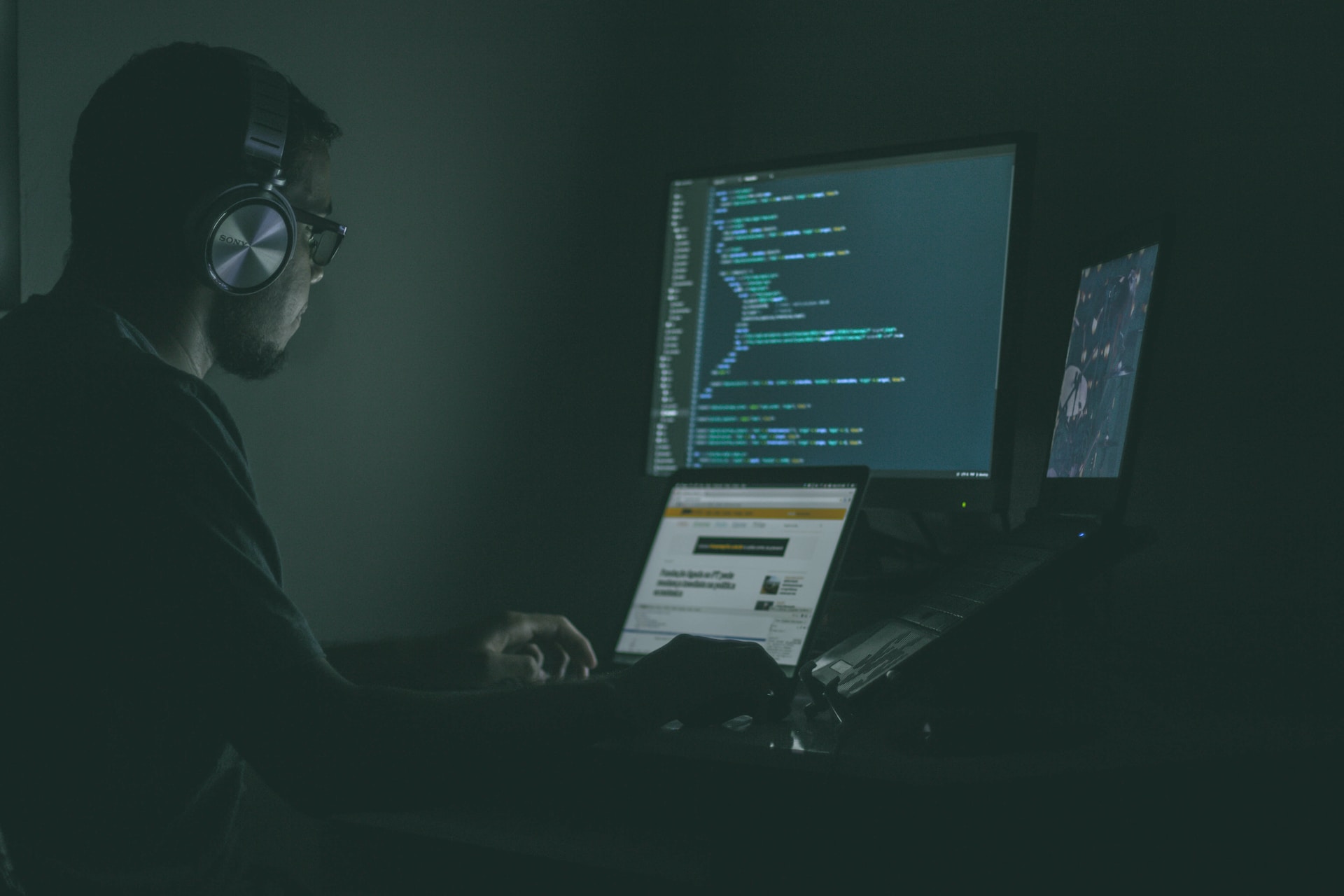 A man wearing headphones while looking at a computer screen with code on it