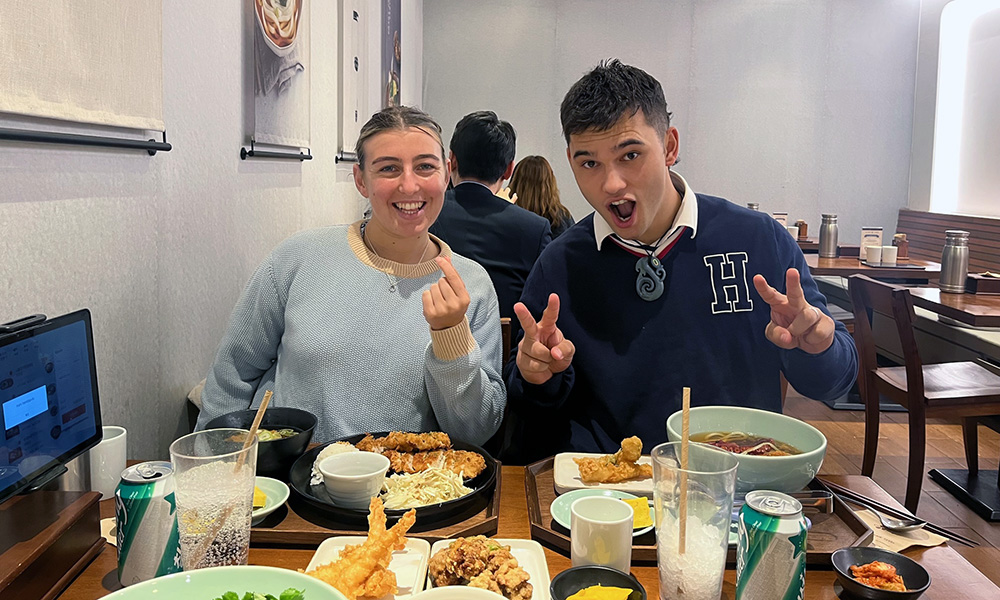 Libby and Brigham posing for a photo over a lunch of fried food and noodle soup