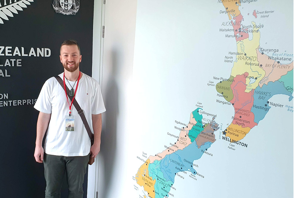 Michael standing beside a large wall-map of New Zealand