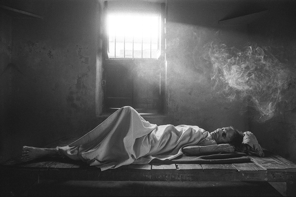 An elderly woman lying under a sheet on boards