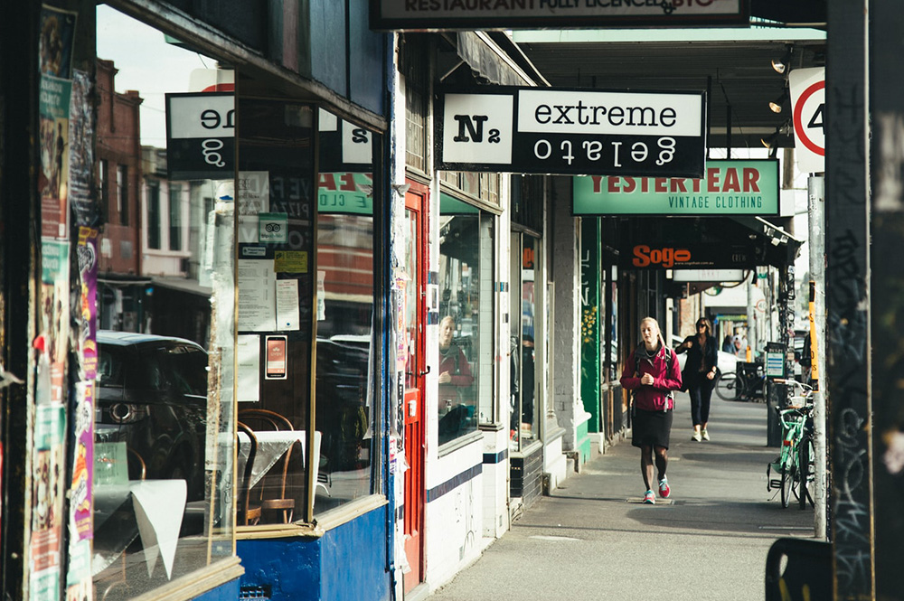 A street with shop fronts and people walking along a footpath