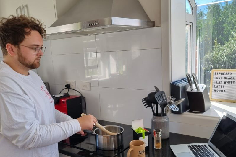 Luke stirring a pot on the stove while looking at his computer