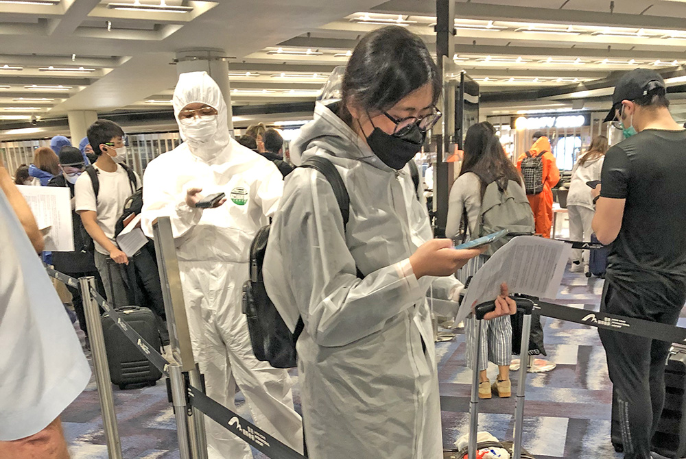 We-Wei standing in a queue at the airport wearing a mask