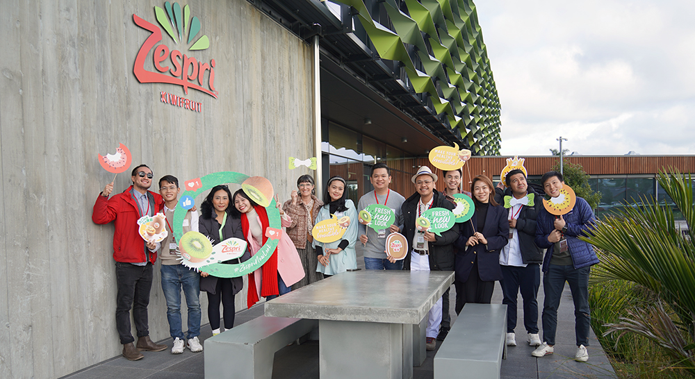 The entrepreneurs lined up for a photo outside the Zespri building holding Zespri kiwfruit cardboard cut outs
