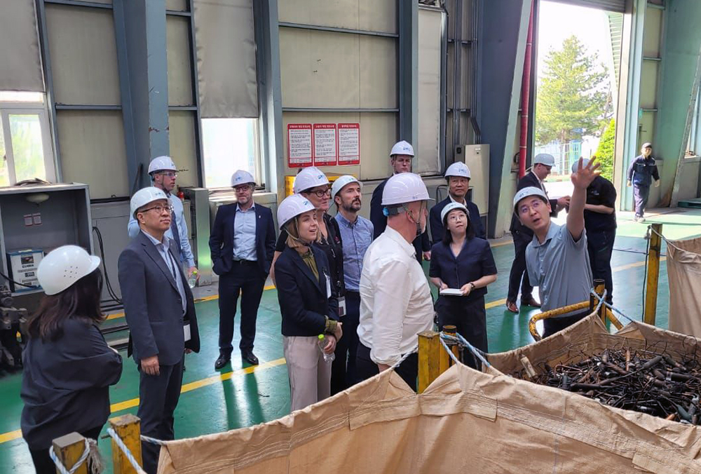 The entrepreneurs wearing hardhats in a recycling plant and as a man addressing them