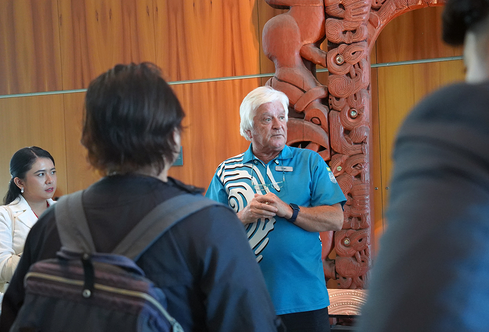 A Te Papa guide speaking to the visiting entrepreneurs in front of a Maori carving