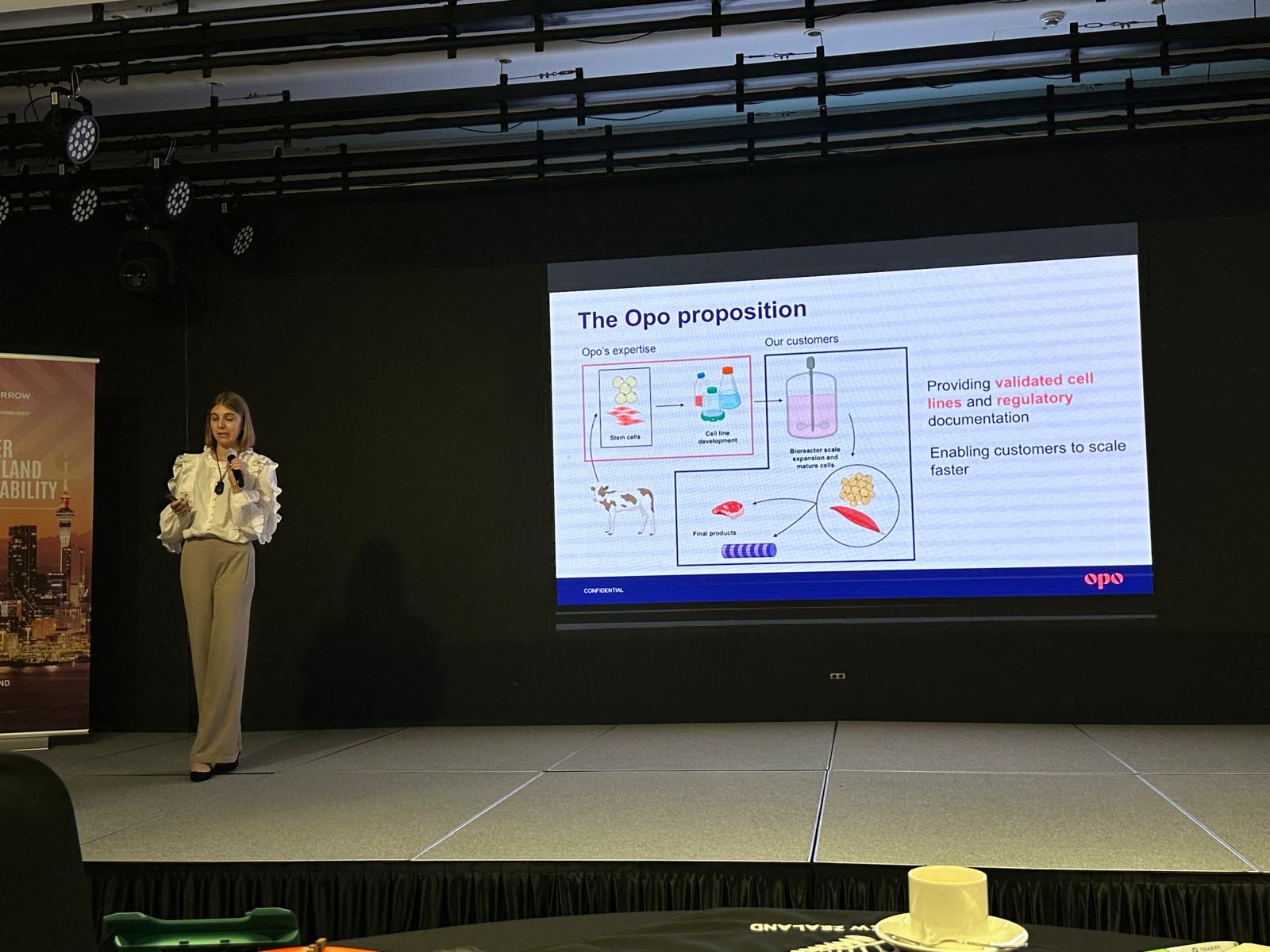 Olivia on stage presenting about Opo, with an infographic about Opo on a screen behind her
