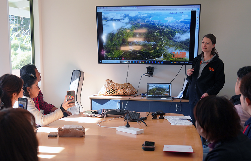 A Zealandia emplyee speaking to group in a room with a video of Zealandia playing in the background