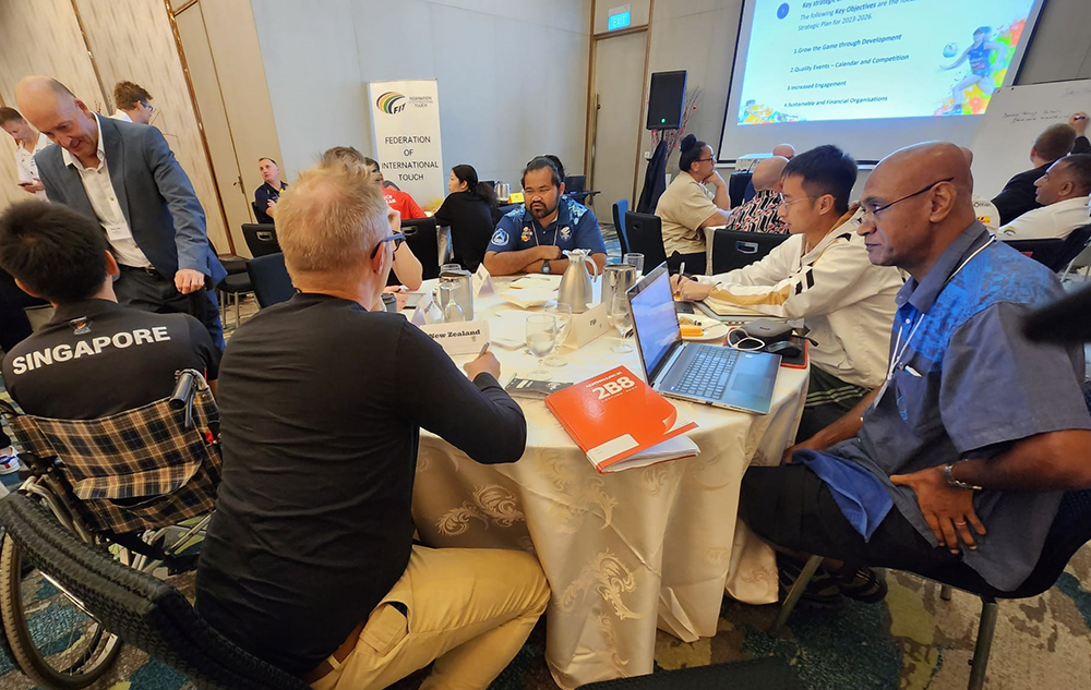 A photo of a room of Touch rugby representatives sitting round tables chatting and taking notes