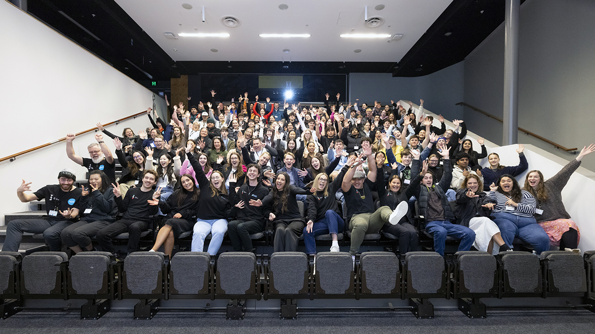 An auditorium of young people waving to the camera for a group photo