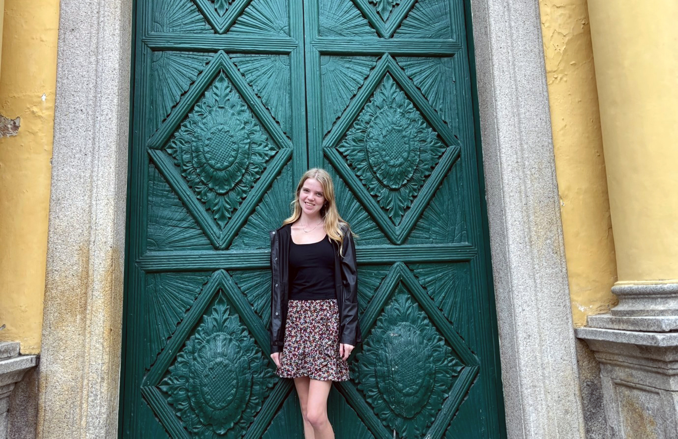 Sian standing outside large, ornate, green doors of an oldbuilding