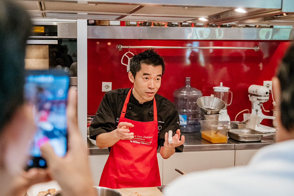 Makoto Tokuyama wearing an Asia New Zealand Foundation apron while addressing a group of festival goers