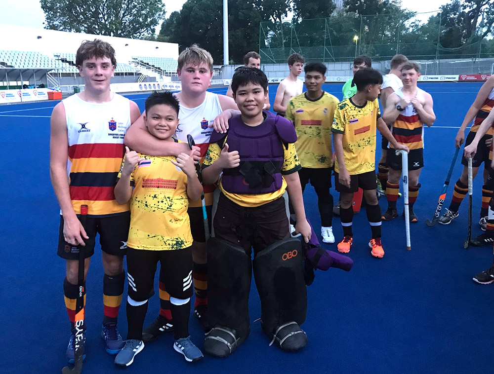 Malaysian and Kiwi players arm in arm on a hockey turf