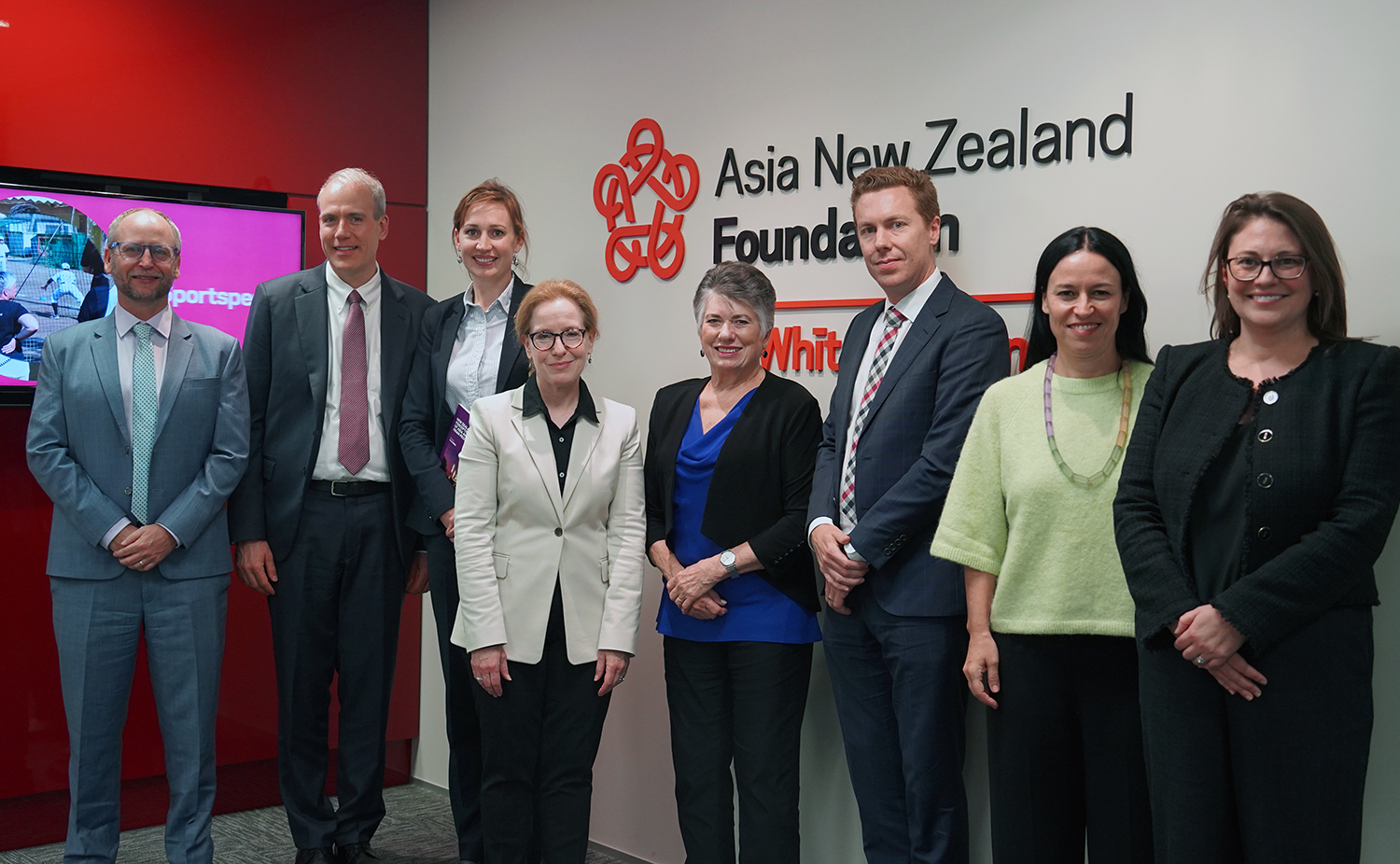 eight people from the Asia Foundation and the Asia New Zealand Foundation posing for a group photo in front of Asia New Zealand Foundation signage