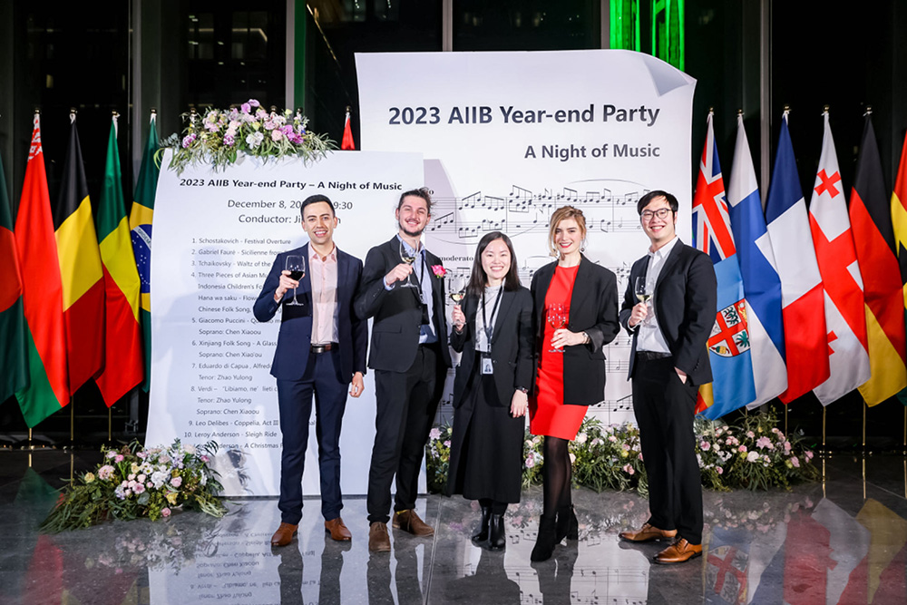 Wesley and four colleagues posing for a photo in front of national flags at a Price Waterhouse Coopers end of year event