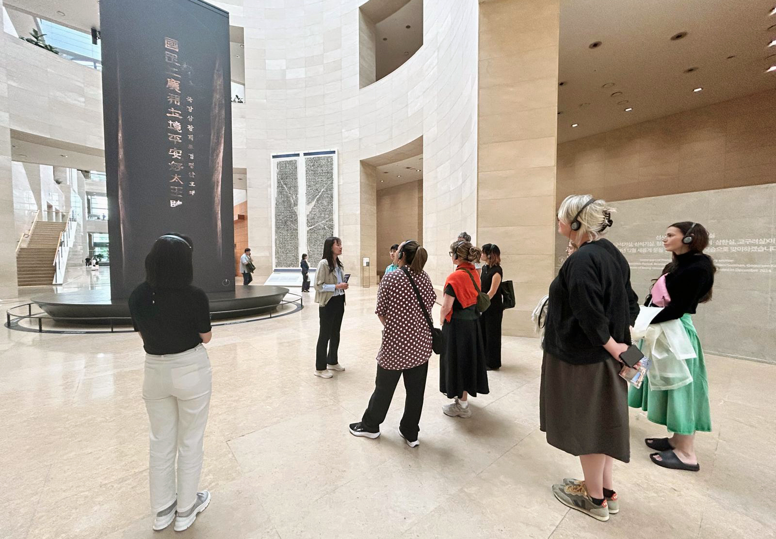 The delegation listening to a woman speak in a gallery