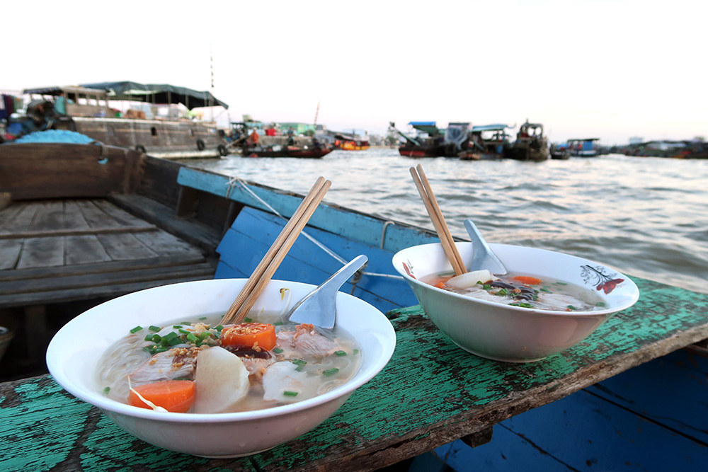 Two bowls of Pho sitting on a bench of a small boat