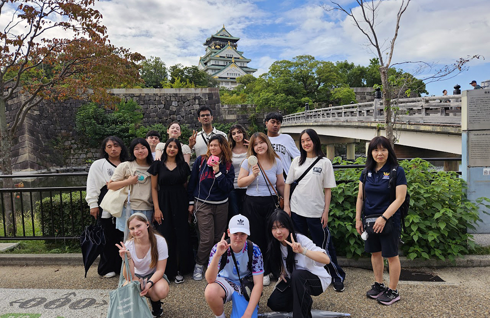 A group photo of the Mount Roskill students standing beside a bridge with a traditional Japanese building in the distance