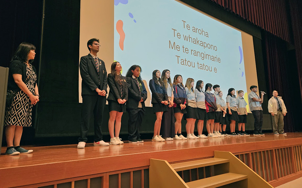 Students standing on stage singing a waita