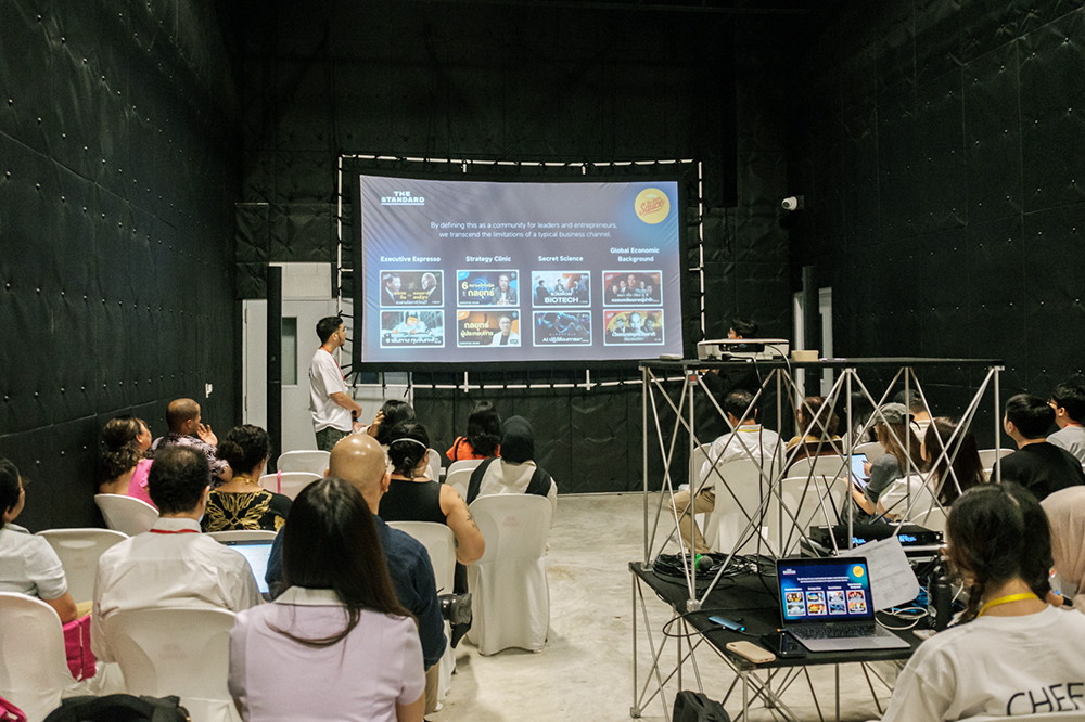 An audience listening to a man speaking to a slideshow projection