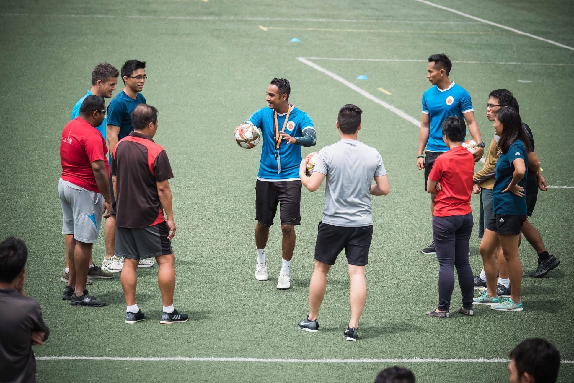 a group of ten people on a football pitch listening to a coach