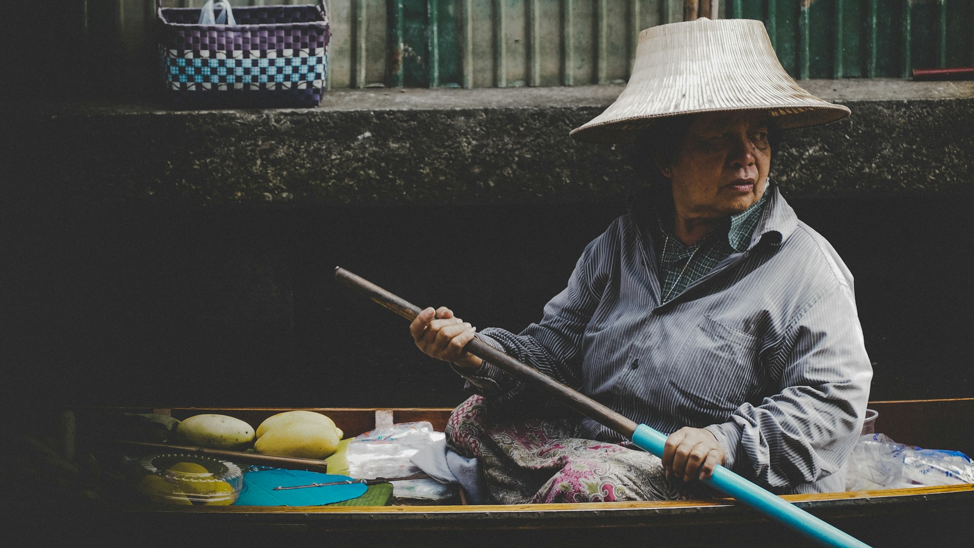An old woman sitting in a shallow boat with fruit