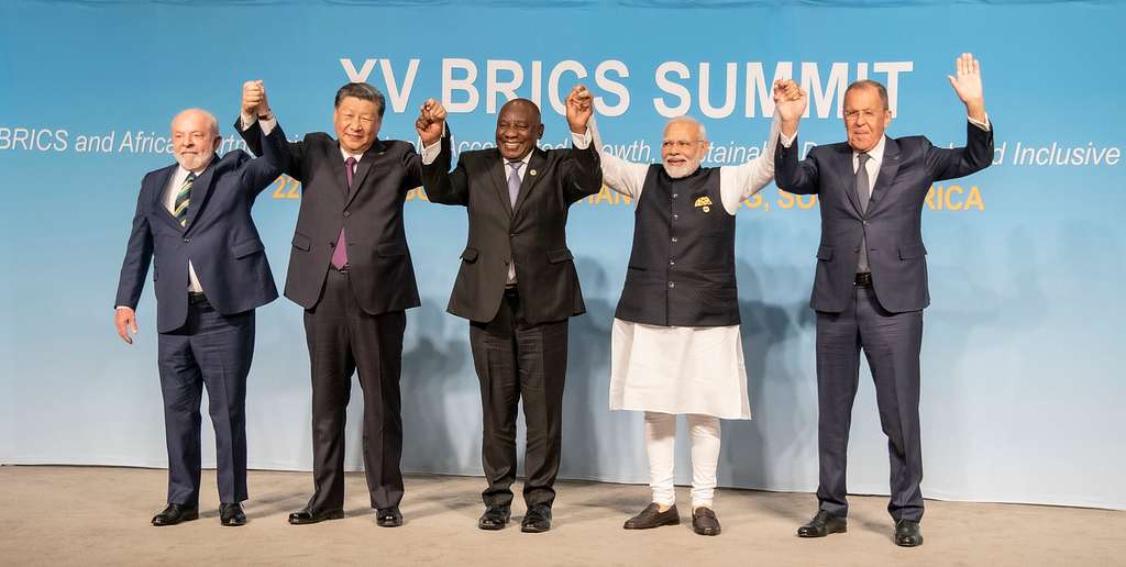 Five national leaders including China's President Xi and India's Prime Minister Modi holding up each others hands with a BRICS Summit billboard behind them