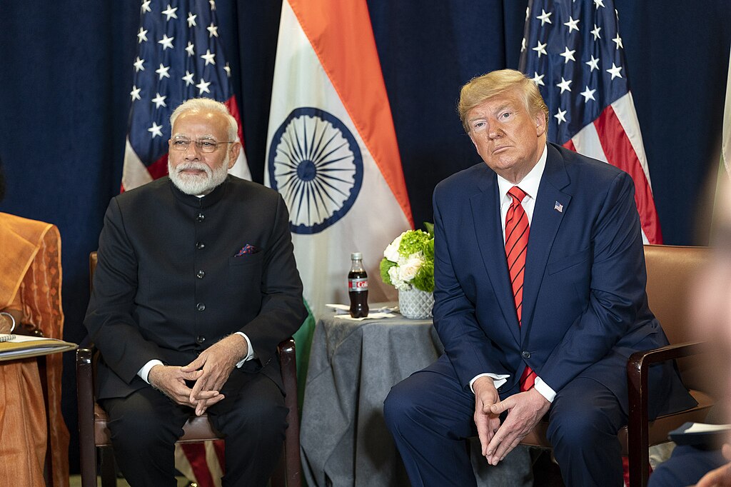 Trump and Modi sitting on stage in front of the United States and Indian flags