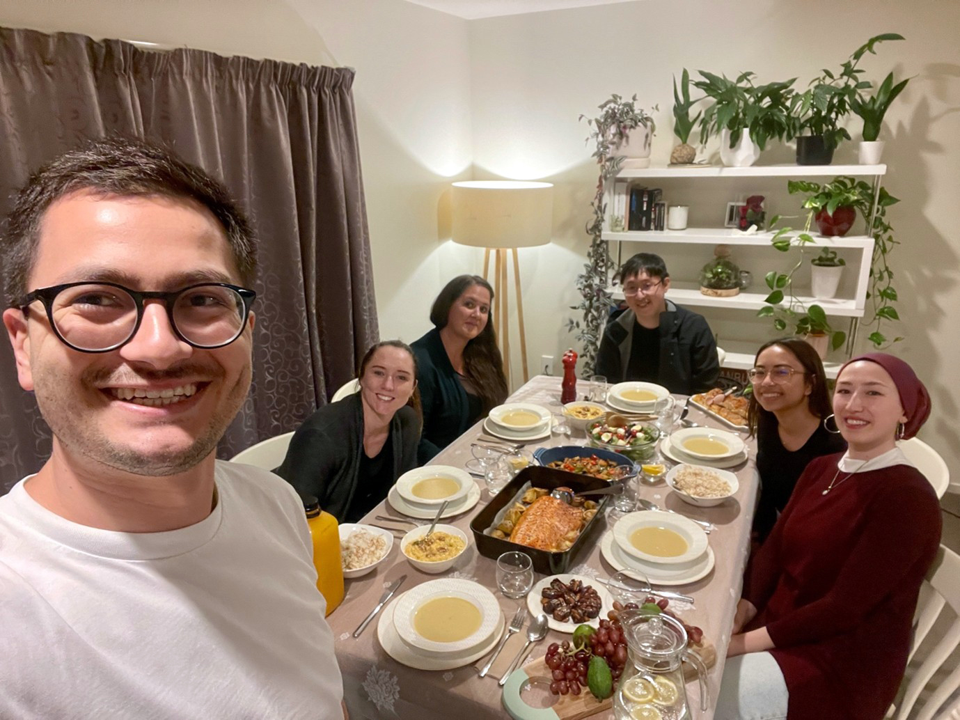 Yasir taking a photo of a dinner gathering with five people sitting at a table with bowls of soup in front of them